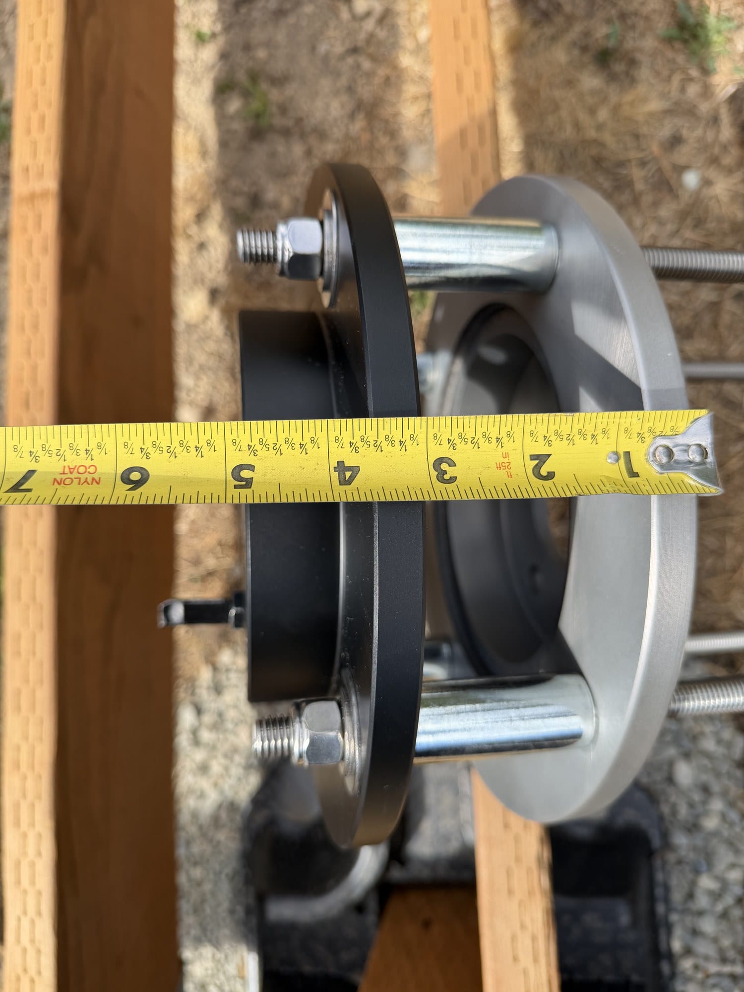 Two brake rotors separated by polished steel tube spacers on threaded rods, with a tape measure across them reading just under five inches.