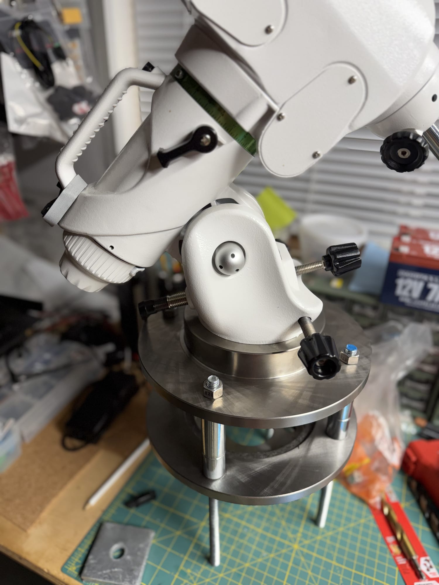 A white equatorial mount sitting on the two-rotor adapter on a workbench during a trial assembly.