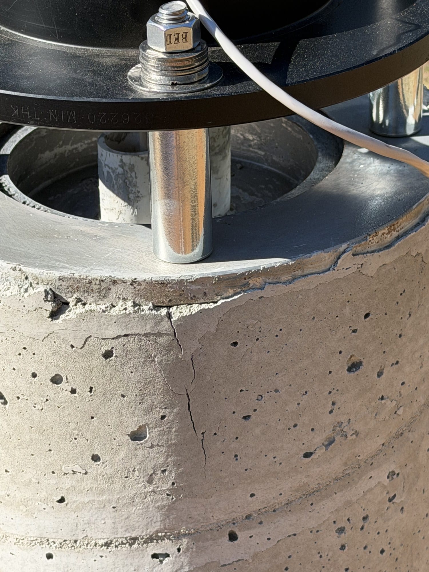 Close-up of the top of a concrete pier showing a fine vertical crack beside one of the threaded rods, with the adapter above.